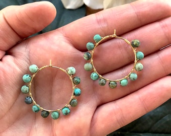 May include: A pair of gold hoop earrings with turquoise beads. The earrings are handmade and feature a simple, elegant design.