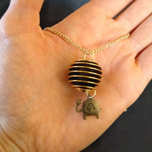 May include: A gold chain necklace with a brown and gold wire-wrapped pendant and a small bronze elephant charm.