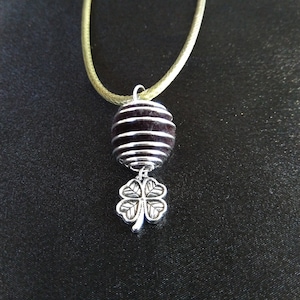 May include: A silver necklace with a dark brown, striped, round bead and a silver four-leaf clover charm.