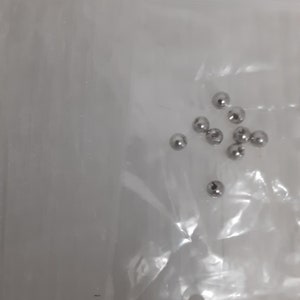 May include: A close-up of a clear plastic bag containing a group of small, silver metal balls.