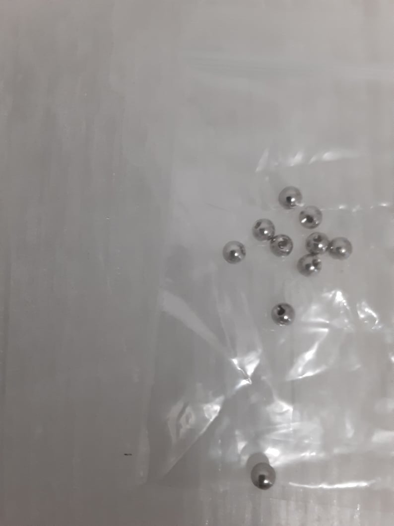 May include: A close-up of a clear plastic bag containing a group of small, silver metal balls.