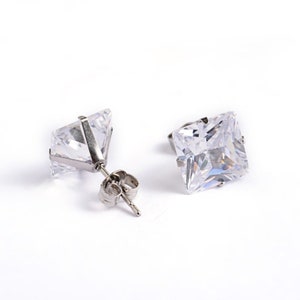 May include: A pair of silver stud earrings with square-shaped clear cubic zirconia stones.