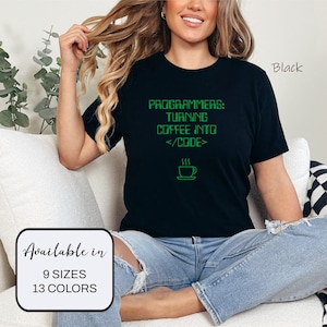 Könnte beinhalten: Ein schwarzes T-Shirt mit dem Text "PROGRAMMERS: TURNING COFFEE INTO </CODE>" in grünem Text. Das Shirt zeigt eine kleine Grafik einer Kaffeetasse mit Dampf, der aus ihr aufsteigt. Der Text "Available in 9 SIZES 13 COLORS" ist in der linken unteren Ecke des Bildes sichtbar. Das Shirt wird von einer Person getragen, die auf einem weißen Sofa sitzt.
