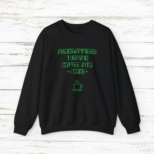 Pode incluir: Camisola preta com o texto verde "PROGRAMMERS: TURNING COFFEE INTO </CODE>" e um desenho de uma ch&aacute;vena de caf&eacute;. A camisola &eacute; de gola redonda.