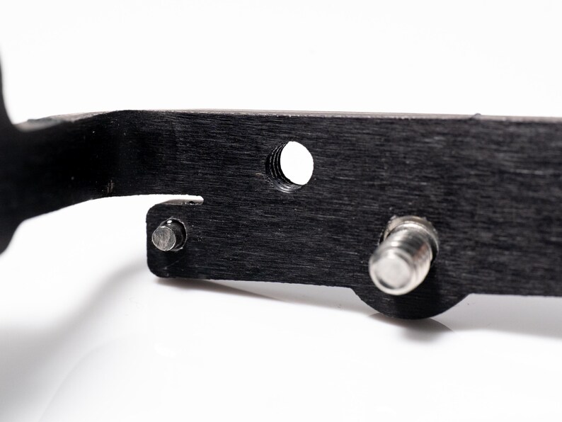 May include: Close-up of a black, textured metal object with a series of holes and silver metal fasteners. The object has a dark, wood-grain appearance and is set against a white background.