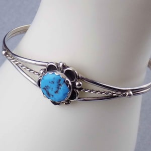 May include: A silver bracelet with a turquoise stone set in a floral design.