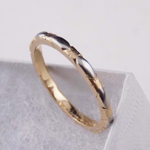 May include: A thin, two-tone metal ring featuring an alternating pattern of polished yellow gold and silver-colored segments. The band has a smooth, rounded profile with distinct, repeating oval-shaped sections that create a textured, segmented appearance.