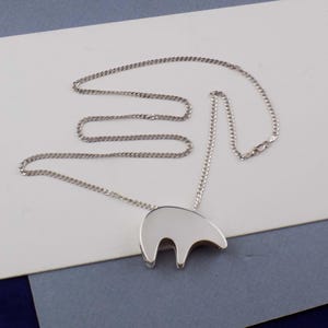 May include: A silver-toned necklace featuring a smooth, polished pendant shaped like a stylized bear silhouette. The pendant is suspended from a delicate, thin metal chain with a standard clasp closure, showcasing a clean and reflective metallic finish.