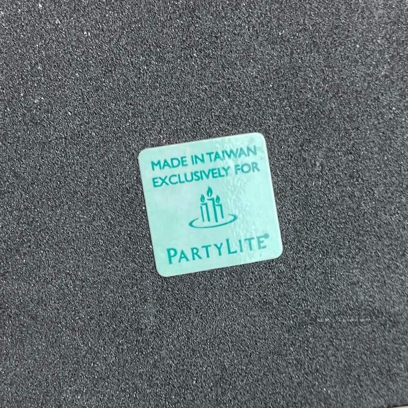 May include: A teal blue square label with the text "Made in Taiwan Exclusively for PartyLite" and a logo of three candles in a circle.