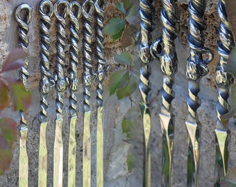 May include: A set of 10 silver metal skewers with twisted handles. The skewers are hanging on a stone wall with green vines.