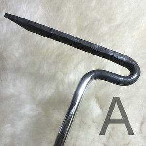 May include: A metal tool with a curved handle and a pointed, flattened end. The handle is polished, while the working end has a textured, dark finish. The letter "A" is visible in the image.