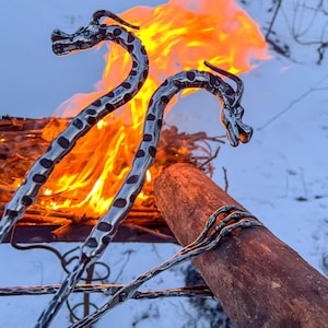 May include: Two metal dragon-shaped fireplace tools with a textured surface, placed over a burning fire pit. The tools are made of metal and have a black finish.