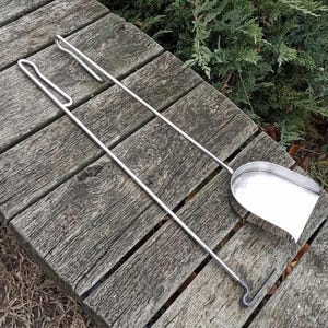 May include: A set of two silver fireplace tools, a poker and a shovel, with wooden handles. The tools are lying on a wooden surface.