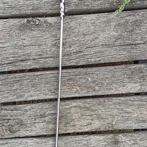 May include: A metal snake hook with a decorative dragon head. The hook is silver with a black and white pattern on the handle. The hook is designed to lift and move snakes safely.