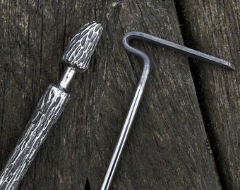 May include: Two metal tools for cooking over a fire. One tool has a textured, rounded head and a long, textured handle. The other tool has a hook shape with a long, straight handle.