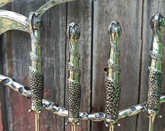 May include: A set of four metal fireplace tools with ornate handles. The handles are silver-colored with a textured, snake-like design. The tools have long, slender, gold-colored shafts and are attached to a decorative silver metal frame.