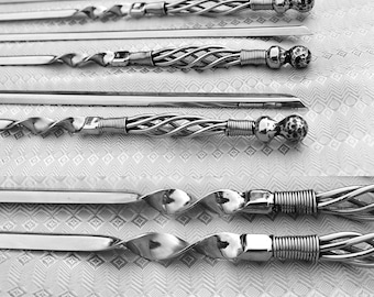 May include: Set of six silver metal skewers with twisted handles and rounded ends. The skewers are arranged in a row on a white patterned surface.