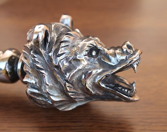 May include: Close-up of a silver bear head sculpture with an open mouth and sharp teeth. The sculpture is detailed and realistic, with fur and facial features clearly visible.