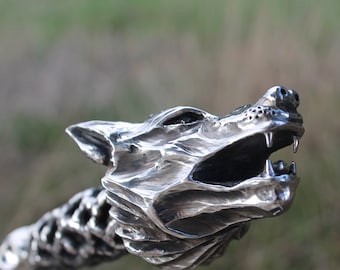 May include: A silver wolf head sculpture with a textured surface and an open mouth. The sculpture is made of metal and has a realistic design.