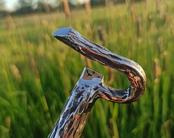 May include: A silver bottle opener with a hammered finish and a unique, curved handle. The opener is made of metal and has a rustic, handmade look.