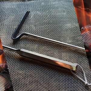 May include: Two metal tools for cleaning a grill. The tools are made of stainless steel and have a brushed finish. The larger tool has a long handle and a curved head with a scraper on one side. The smaller tool has a shorter handle and a flat head with a scraper on one side.