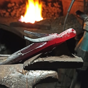 May include: A blacksmith's workshop scene with a piece of red-hot metal held in tongs, resting on an anvil. The metal glows brightly, and a forge fire blazes in the background, creating a dramatic contrast.
