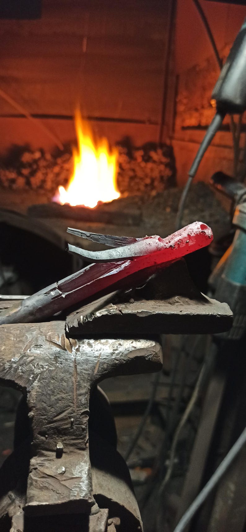 May include: A blacksmith's workshop scene with a piece of red-hot metal held in tongs, resting on an anvil. The metal glows brightly, and a forge fire blazes in the background, creating a dramatic contrast.