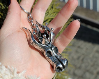 May include: Silver-toned metal keychain featuring a detailed dragon head with a crown on top. The dragon's head is textured and has a realistic design.