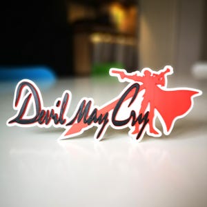 May include: A 3D printed red and black Devil May Cry logo with a silhouette of a character holding a sword.