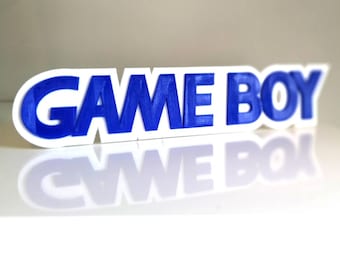 Puede incluir: Un letrero blanco impreso en 3D con las palabras "GAME BOY" en letras azules.