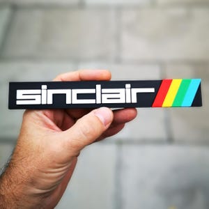 May include: Black rectangular sticker with the word "Sinclair" in white letters and a rainbow stripe on the right side.