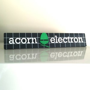 May include: A black and white sign with a green acorn logo and the text "acorn electron" in white letters.
