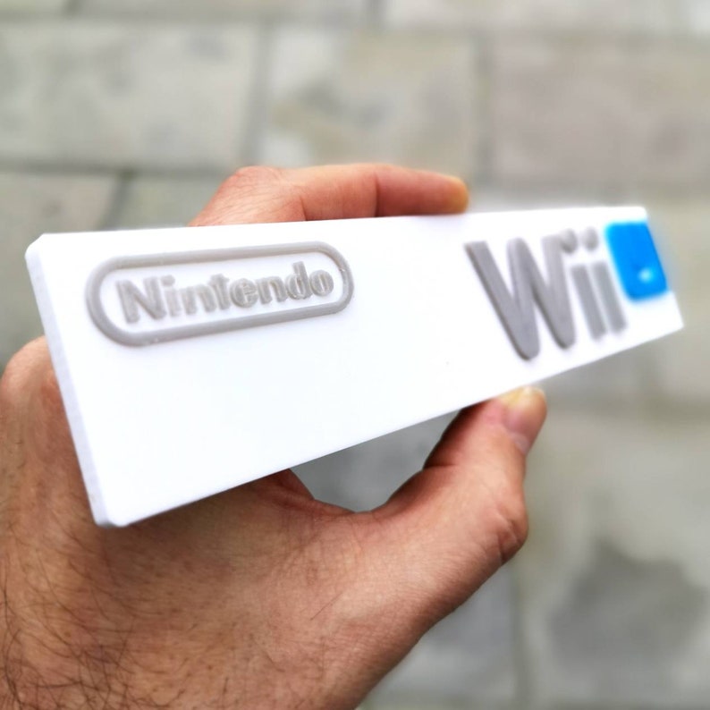 May include: A white Nintendo Wii console with the Nintendo logo and the word "Wii" in gray lettering. The "i" in Wii is blue.