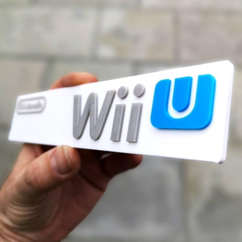 May include: A white plastic sign with the words "Wii U" in gray and blue lettering. The "U" is a blue square with a white outline.