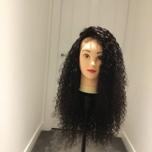 May include: A black curly human hair wig on a mannequin head. The wig is styled with a side part and has loose curls.
