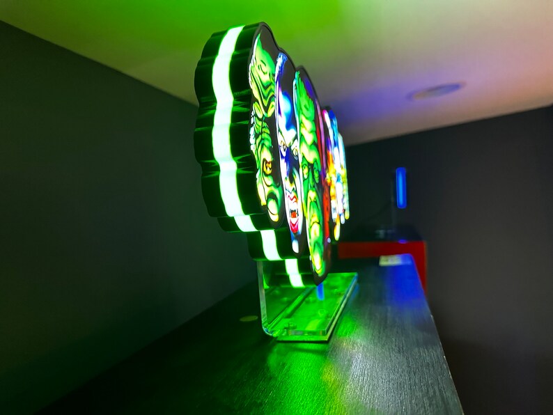 May include: A green, black and white 3D printed light-up display featuring the faces of four classic horror movie monsters. The display is on a clear acrylic base.