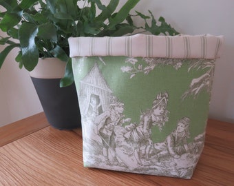 May include: A green fabric storage basket with a white and green striped top. The basket features a black and white print of children playing in a woodland setting.