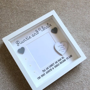 以下が含まれることがあります： 「Auntie and Uncle」の文字が筆記体で書かれた白いシャドウボックスフレーム。フレームには写真用の空白スペース、2つの灰色のハート、そして「Lots of Love Cillian」の文字が入ったハート型の装飾が含まれています。「I'm as lucky as can be, the best auntie & uncle belong to me」の文字も含まれています。