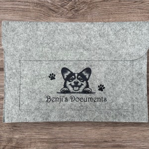 May include: Grey felt document folder with a black and white illustration of a corgi dog peeking over the top. The text "Benji's Documents" is printed below the dog.