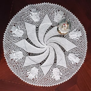 May include: White crocheted doily with a spiral design and a snowflake pattern around the edge.