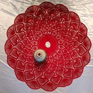 Puede incluir: Falda de árbol de Navidad de crochet rojo con un adorno de cerámica blanco y verde en el centro.
