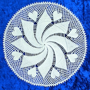 May include: White crocheted doily with a spiral design and a scalloped edge. The doily is made of delicate, intricate stitches and has a classic, elegant look.