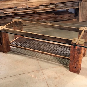 May include: A rustic coffee table with a glass top and a metal wire shelf. The table is made from reclaimed wood and has a natural wood finish.