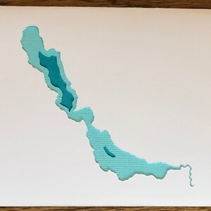 May include: A light blue paper cutout of a lake with a smaller lake inside. The cutout is on a white background.