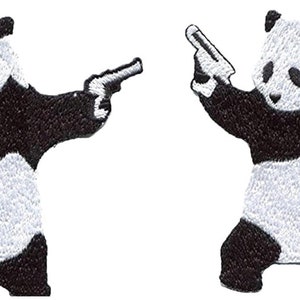 May include: Embroidered patch featuring a panda bear in black and white, holding two toy guns. The panda is standing with its arms outstretched, and the guns are pointed outwards. The patch has a detailed, textured appearance.