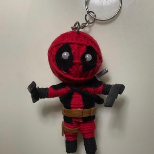 Puede incluir: Llavero de muñeca de hilo rojo y negro de Deadpool con un cinturón marrón y un anillo de llave plateado.