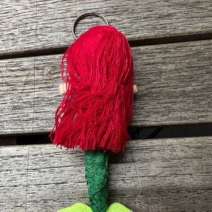 May include: A red haired mermaid keychain with a green tail and light green fins. The keychain has a silver ring.