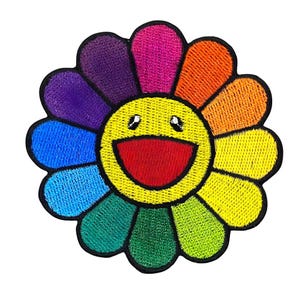 May include: Embroidered patch featuring a smiling flower design. The flower has a yellow center with a red mouth and black eyes. The petals are a rainbow of colors, including purple, pink, orange, yellow, green, and blue. The patch has a black border.