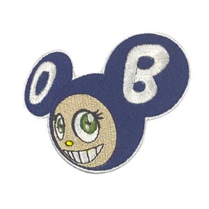 May include: Embroidered patch featuring a cartoon character with a smiling face, green eyes, and a navy blue head with the letter "B". The character's face is tan with a yellow nose and white teeth.