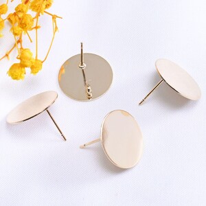 May include: Four gold-colored, round stud earring components are displayed against a white background. Each component features a flat, circular disc with a post for insertion into the ear. The earrings are a simple, elegant design.